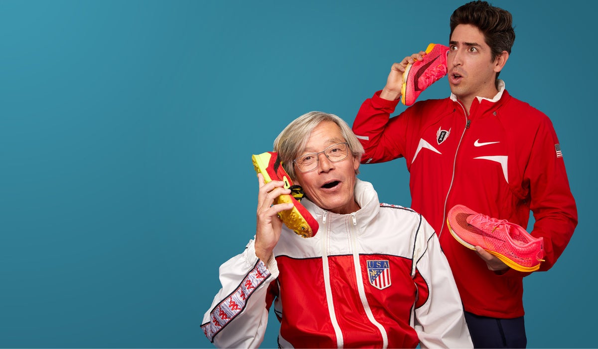 Two men in red and white athletic jackets humorously use running shoes as phones against a blue background, conveying a playful and quirky mood.