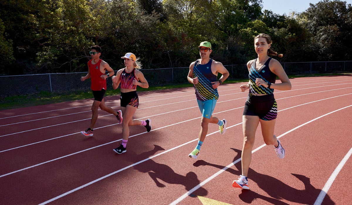 Four athletes jog on a sunlit track surrounded by trees, wearing colorful athletic gear and expressing determination and focus.