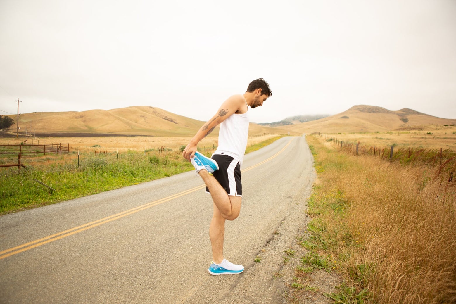 Male runner wearing HOKAs stretching his leg on an empty open road