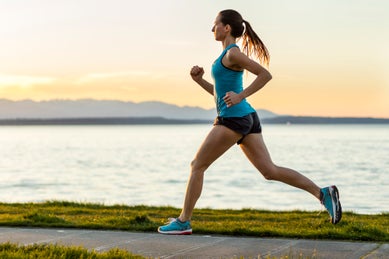 Woman running paved path by lake with foothills in distant background across the water