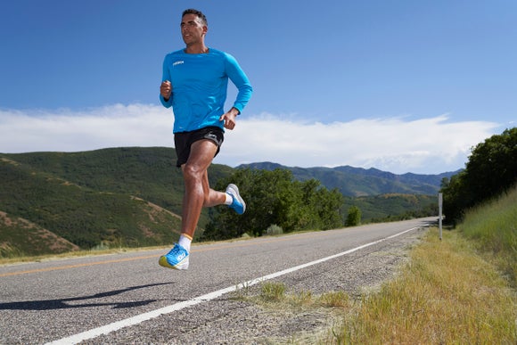 Male runner wearing HOKA apparel and shoes, running on the road overlooking hillside