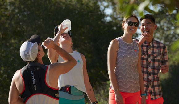 Two runners drinking water while two other runners are standing and smiling