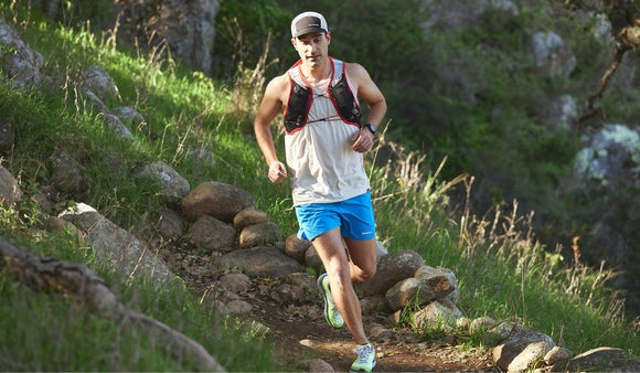 Male runner wearing a hydration vest, tank and shorts while trail running