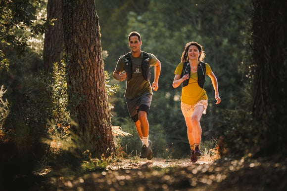 Man and woman running on the trails wearirng hydration vests