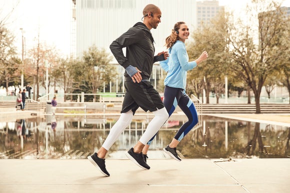 Man and woman running by a fountain wearing earbuds 