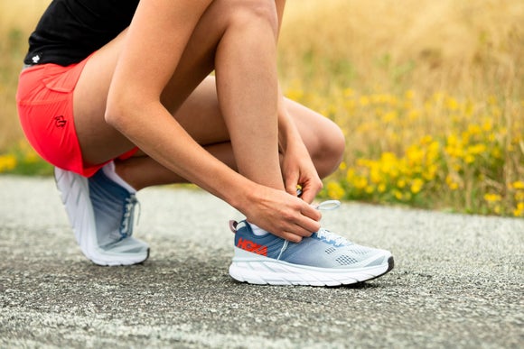 A runner tying the laces on her HOKA Clifton 6 running shoes