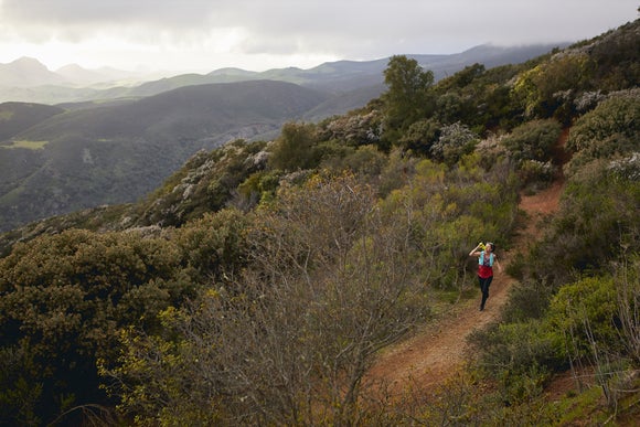 female trail runner running in the hills and drinking from a bottle