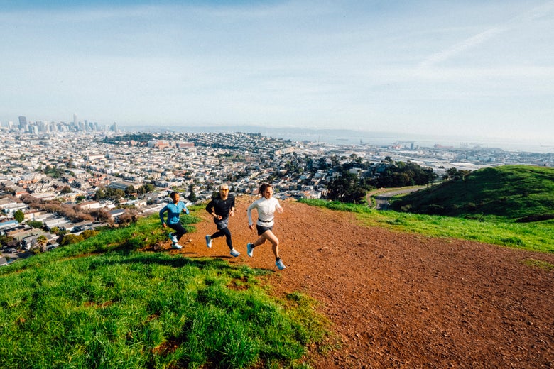 Runners on a scenic mountain trail with a city in the background