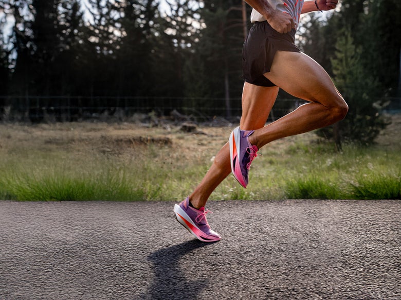 Athete running down a road wearing the Kipstorm Lab in a pink colorway. 