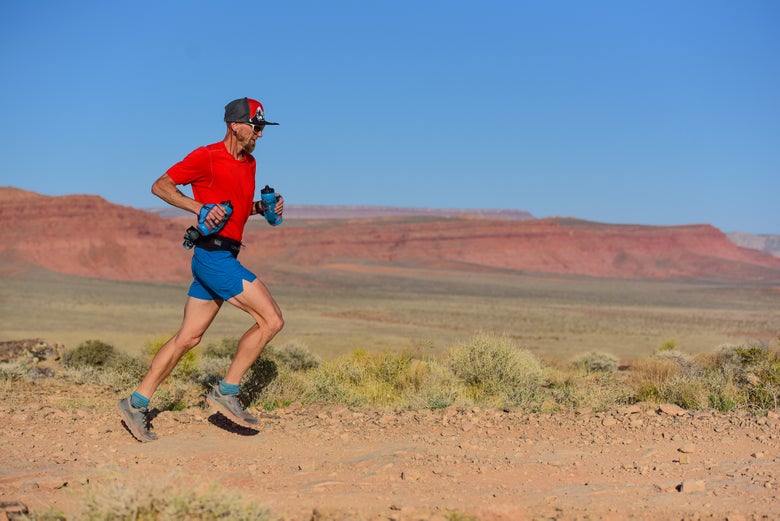 Trail runner wearing Altra trail running shoes jogging on easy trail carrying handhelds