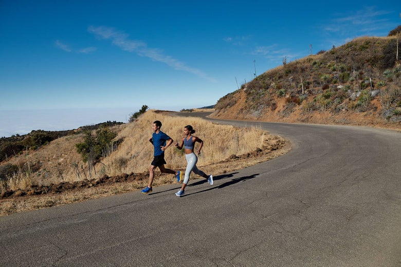 Image of a male and female runner running on a winding road in the hills