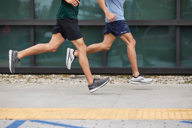 Two men in athletic gear are running side by side on a concrete pathway. They wear shorts and T-shirts, conveying a sense of movement and fitness.