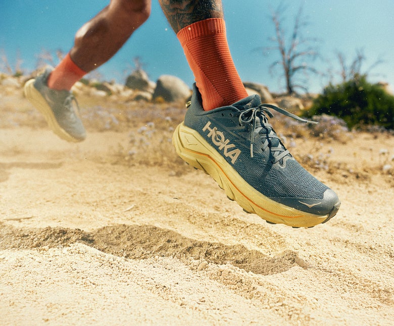Image of runner running through sandy trail wearing the HOKA Challenger 8 in a dark blue colorway