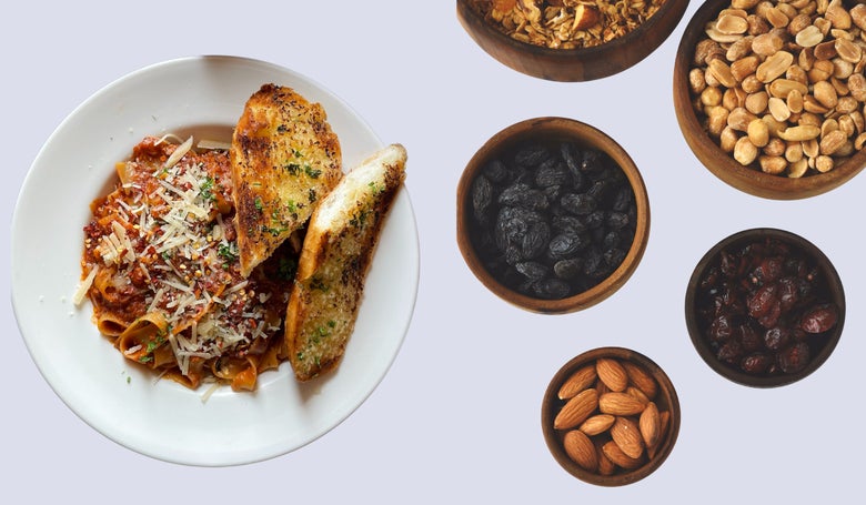 A plate of pasta topped with tomato sauce and cheese, served with two slices of garlic bread. Nearby are bowls of nuts, raisins, and dried fruits.