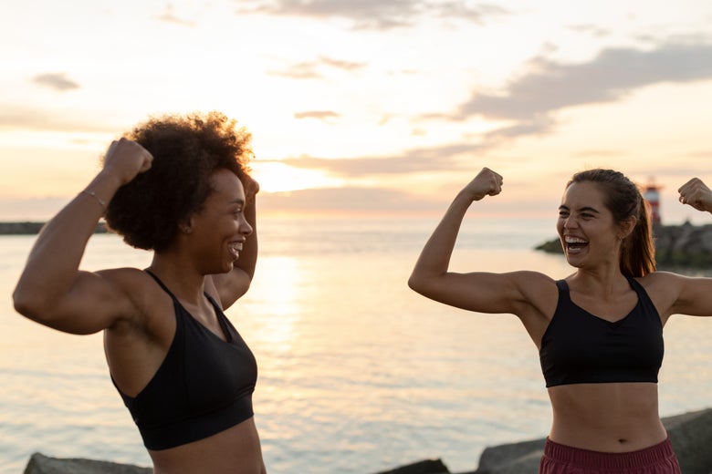 Two women wearing sports bras and flexing their muscles