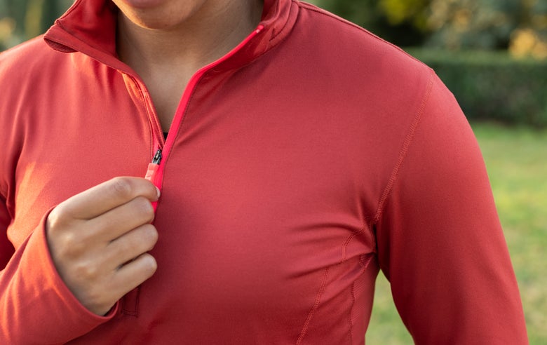 Close up of a long sleeve half zip top with the wearer holding the zipper tab