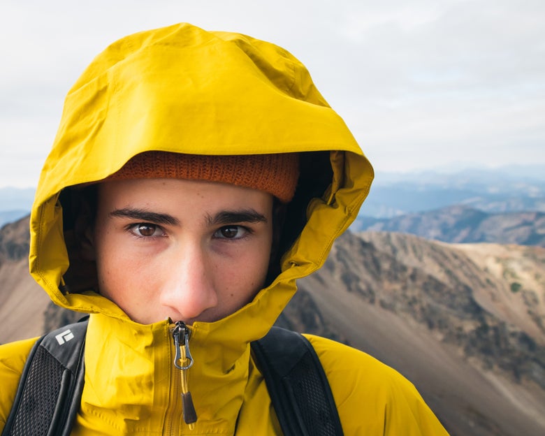 A guy wearing a yellow waterproof jacket with hood against the view of the mountains