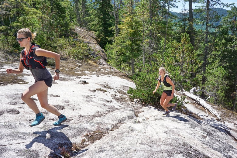 Two runners wearing trail shoes on forest trail with rocky terrain