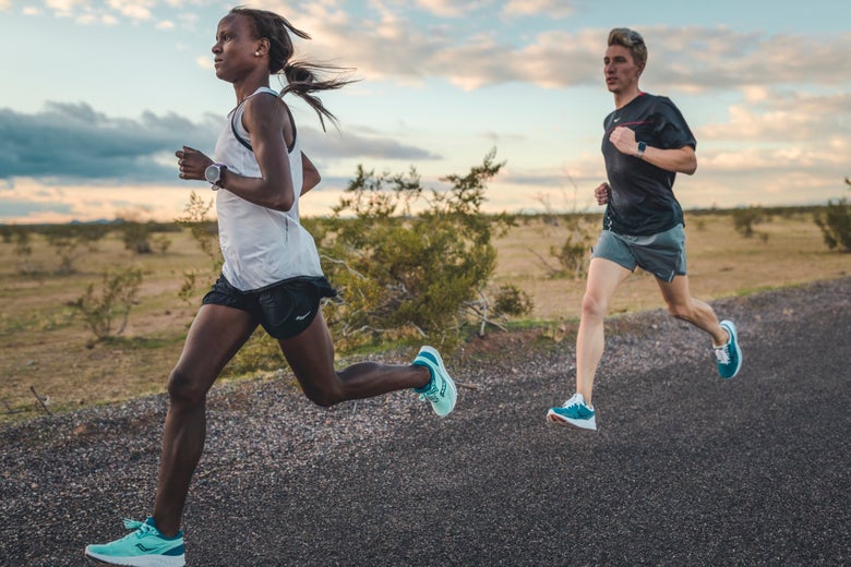 Female runner leading in front of male runner on gravel road with sunset-lit sky
