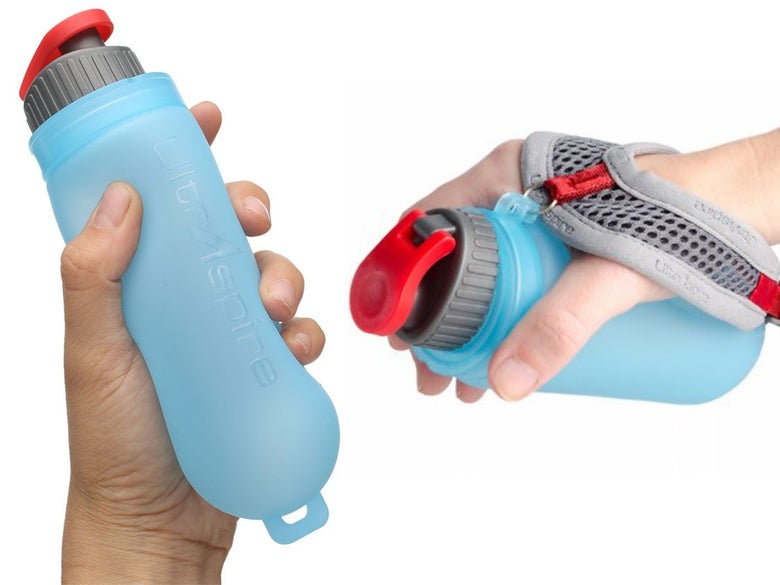 A blue, handheld collapsible water bottle with a red spout is shown in two hands. One hand holds it directly, while the other uses a gray strap.