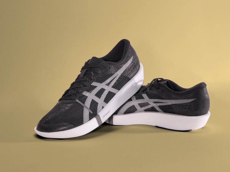 a pair of ASICS METASLEEK shoes in the black and white colorway, on a tan studio background