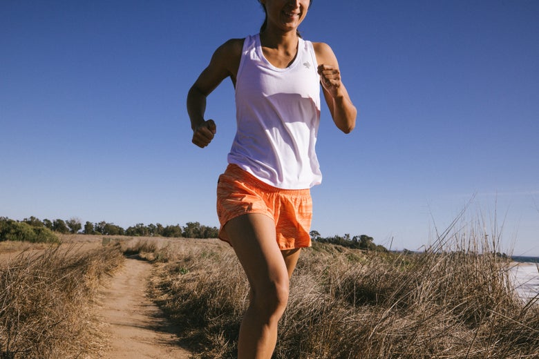 Woman running outdoors in rabbit orange colored summit chaser shorts