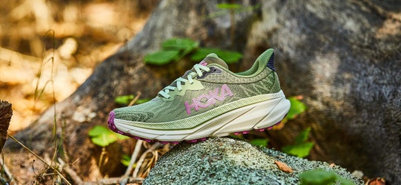 Women's HOKA Challenger shoe in olive color on top of a rock in the woods