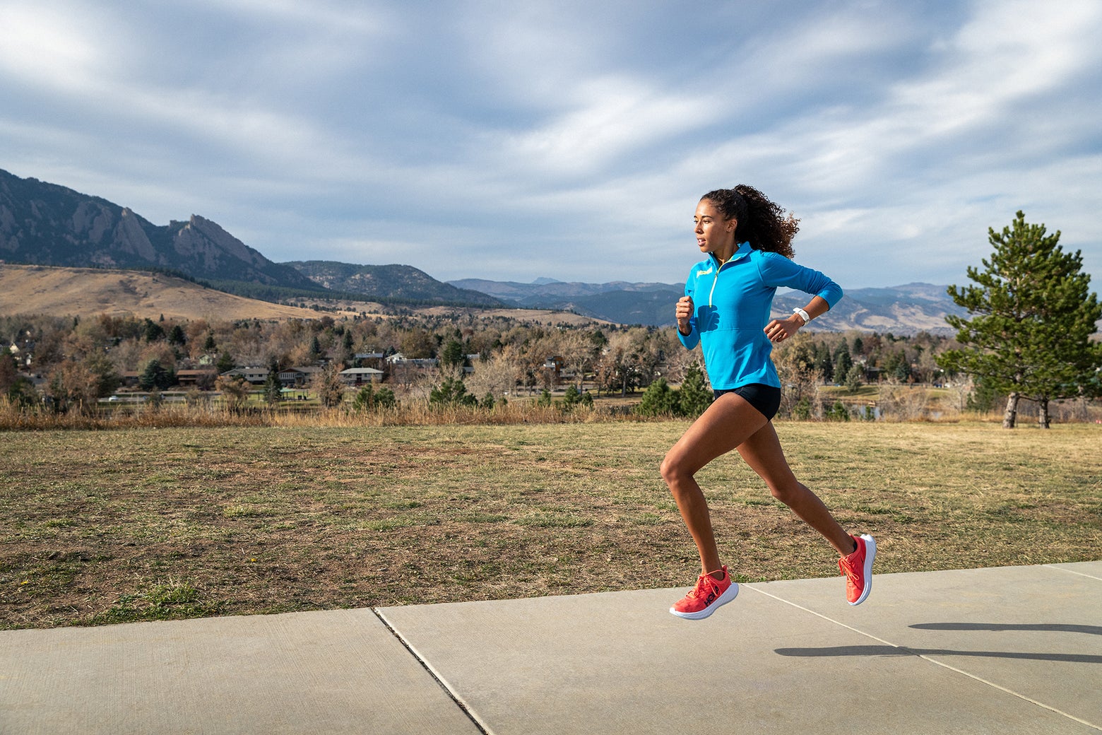 Female runner wearing a blue HOKA half zip and black shorts