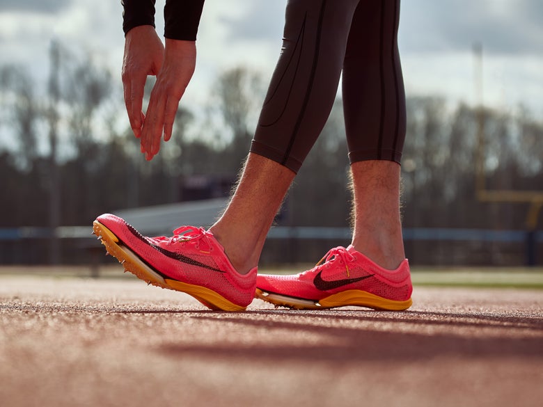 Close up of the feet of a runner on a track wearing neon pink Nike Zoom Victory track spikes.