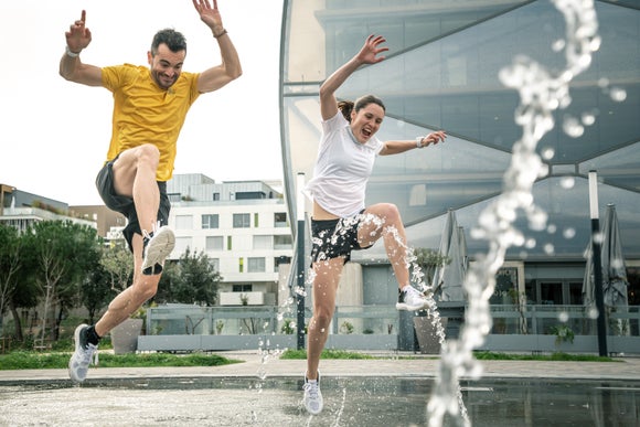 man and woman wearing shorts and t-shirts jumping over a water fountain