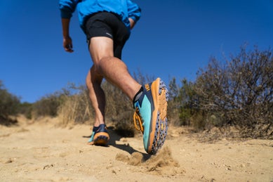 Man running in turquoise Hoka Zinal trail shoe on rocks