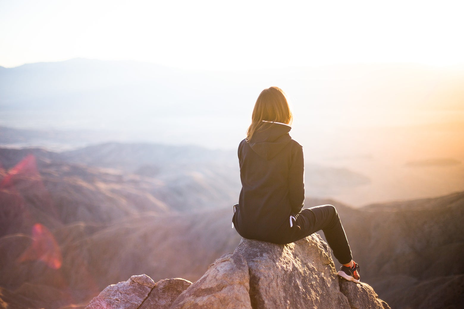 Woman sitting on top of a mountain overlooking a sunrise