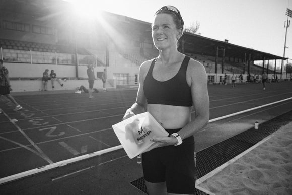 Black and white photo of a female athlete holding a Maurten bag with energy gels on a track field
