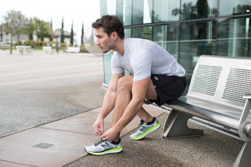 Male runner sitting on a bench tying his shoe laces