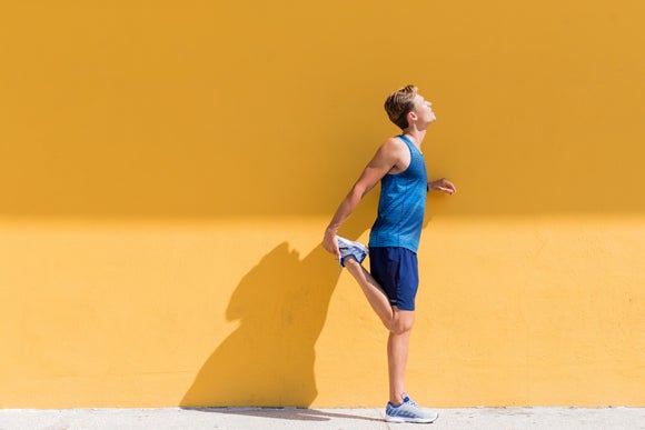 A runner stretching by a yellow wall