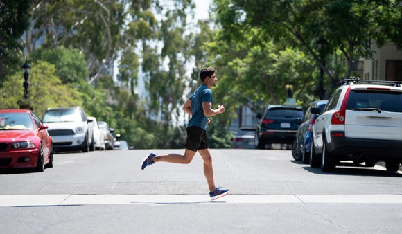 man running on the street alongside parked cars in a blue shirt and black shorts