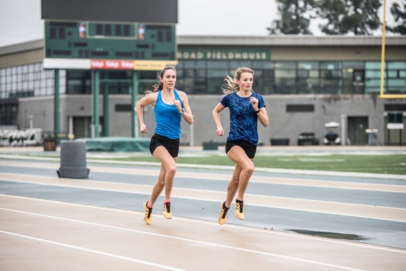 two women running on track while wearing spikes