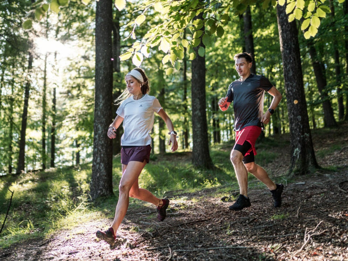 man and woman trail running downhill wearing short sleeve shirts and shorts
