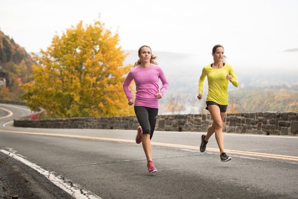 two female runners running on a curvy road wearing long sleeve shirts in autumn