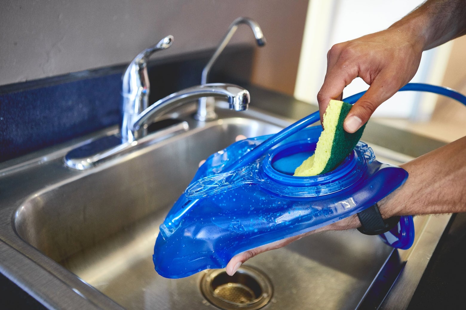 Man washing a hydration pack bladder over the sink