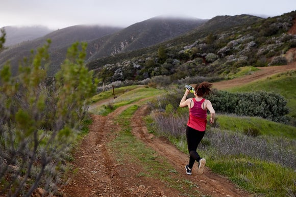 female runner drinking from a bottle while running on the trail